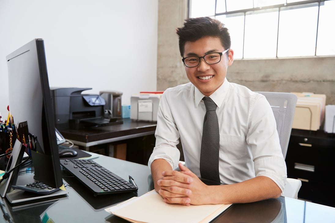 Young Asian Male Professional at Desk Smiling to Camera